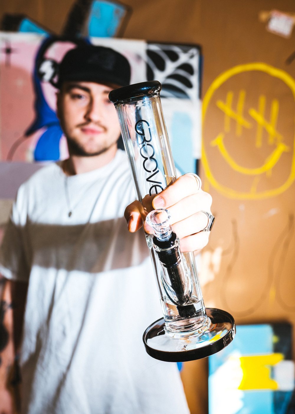 Man in a white tee holding out a GROOVE straight tube toward the camera in front of street art