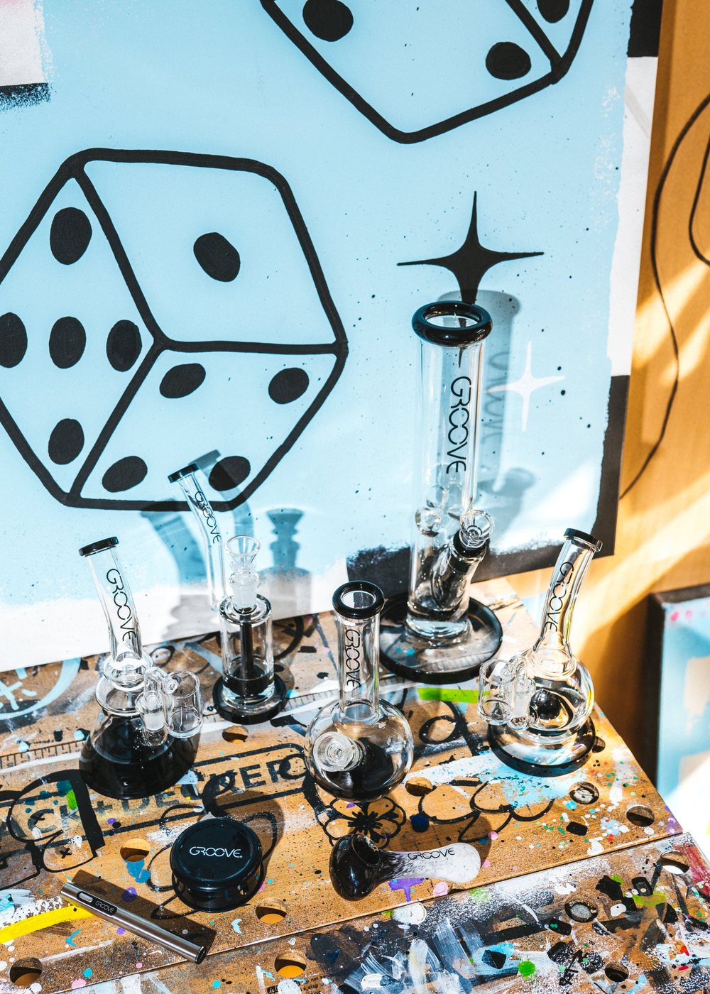The GROOVE lineup of glass, grinder, hand pipe and one-hitter on a paint-splattered artist table